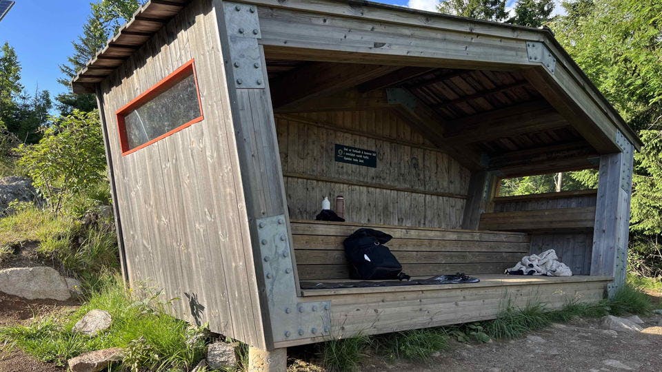 A wooden shelter with black backpack inside